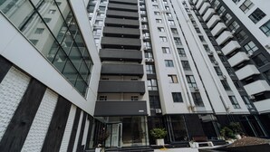Un immeuble moderne à plusieurs étages, doté d’une façade en verre, de balcons et d’une entrée centrale avec des marches.