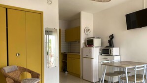 Ein gemütlicher Raum mit einem Bett, einem Esstisch mit Stühlen, einer Küchenzeile mit Mikrowelle und kleinem Kühlschrank, einem Korbsessel und einem an der Wand befestigten Fernseher.