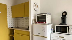 Eine kleine Küche mit gelben Schränken, einem weißen Kühlschrank, einer Mikrowelle und einer Kaffeemaschine.