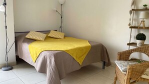 Ein ordentlich eingerichtetes Schlafzimmer mit einem Bett, Nachttischlampen, einem Sessel und einem kleinen Regal mit einer Pflanze.