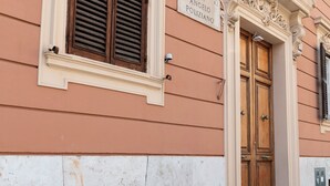 Une façade d’immeuble avec une enseigne indiquant « VIA ANGELO POLIZIANO », une porte en bois et une fenêtre avec des volets.