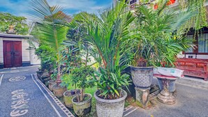 A courtyard with potted plants, a traditional building with a red door, and a tiled walkway.