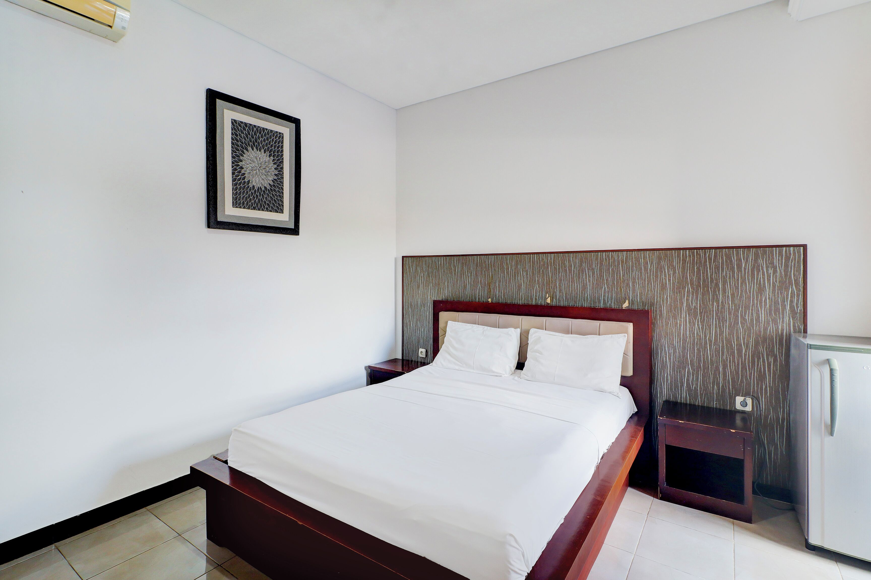 A neatly made bed with white linens, a wooden headboard, a small bedside table, and a wall-mounted picture.