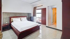 A hotel room with a wooden bed, a nightstand, a small refrigerator, and a view of the outside balcony.
