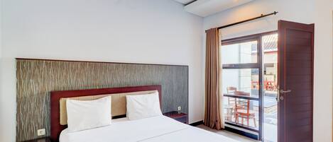 Habitación de hotel con una cama grande, cabecera de madera y vista al área de estar exterior a través de la puerta de vidrio.