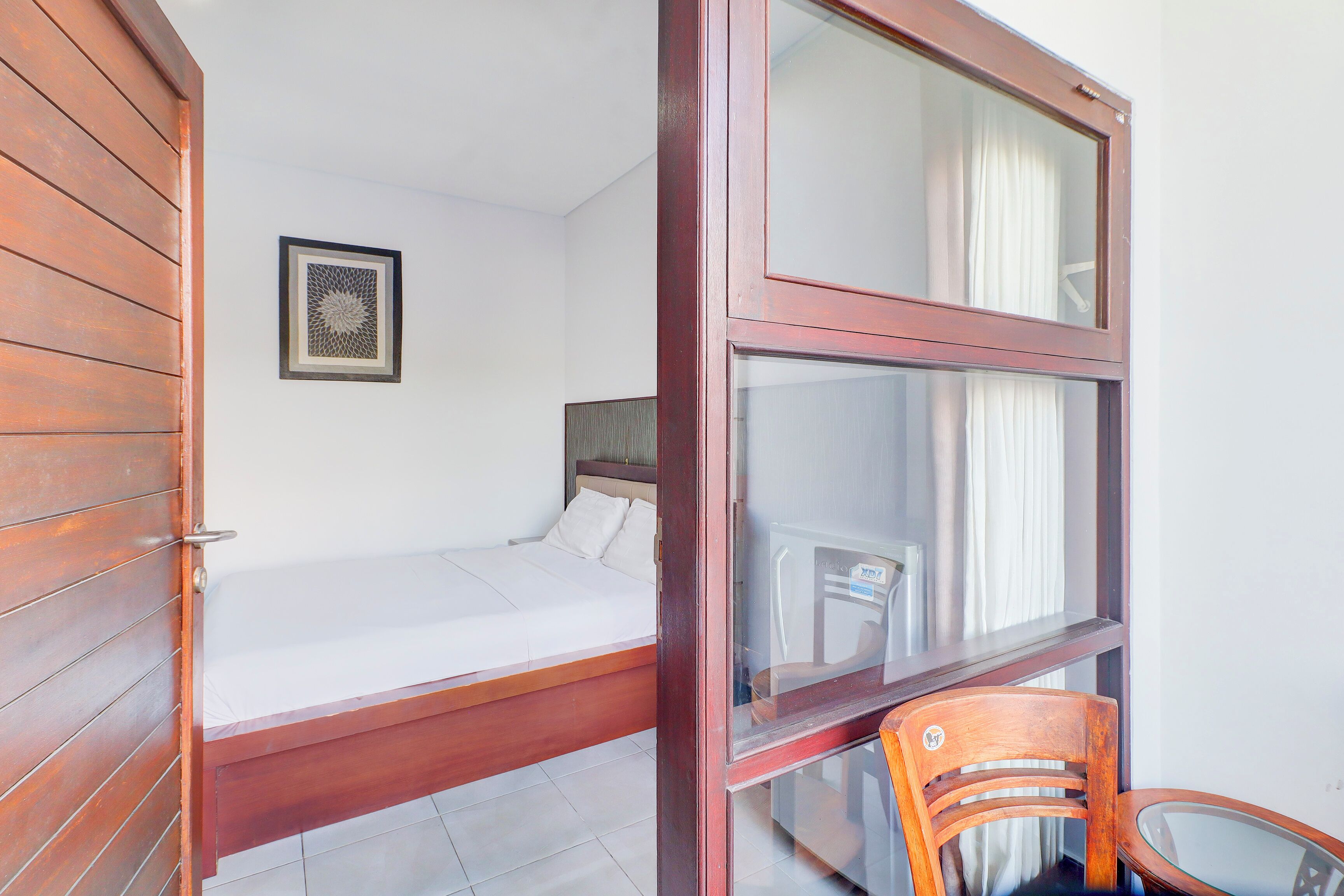A room with a wooden bed, a framed picture on the wall, and a glass table with a chair.