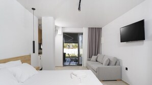 A modern hotel room with a bed, a sofa, a TV, and a view of the outdoors. - Rigas Boutique Rooms (Pefkochori)