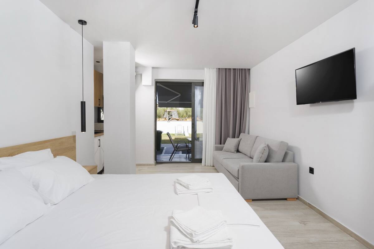 Una habitación de hotel moderna con una cama, un sofá, un televisor y vistas al exterior.