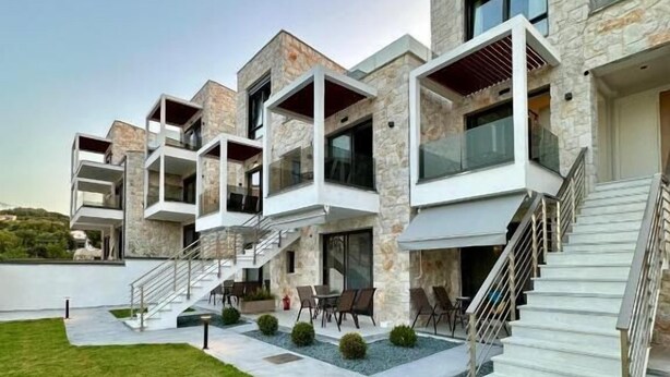 A modern multi-story residential building with balconies, a landscaped lawn, and a staircase leading to the entrance. - Rigas Boutique Rooms (Pefkochori)