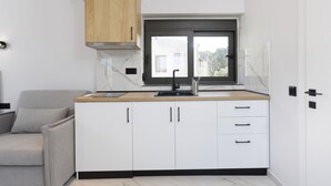 A compact kitchen with white cabinets, a wooden countertop, a black sink, and a window above the sink. - Rigas Boutique Rooms (Pefkochori)