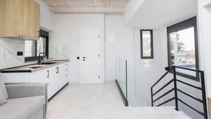 A modern kitchen with white cabinets, a wooden ceiling, and a view of the outside through a large window. - Rigas Boutique Rooms (Pefkochori)