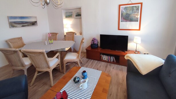 A living room with a dining table, chairs, a sofa, a TV, a bookshelf, and a painting on the wall. - 700 m from the beach, affordable and elegant. We are family and pet friendly (Heringsdorf)