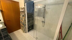 A glass-enclosed shower with a handheld showerhead, a towel rack, and a door with a wooden frame. - Cleo Limone (Falconara Marittima)