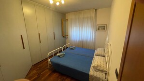 A bedroom with two beds, a wardrobe, a mirror, and a window with curtains. - Cleo Limone (Falconara Marittima)