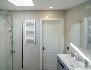 Une salle de bain moderne avec une douche à l’italienne en verre, une porte blanche et un grand miroir au-dessus du lavabo.