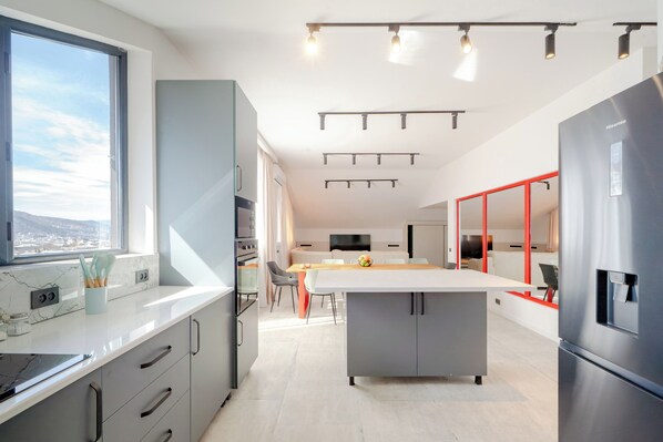 Une cuisine moderne dotée d’un grand îlot central, d’appareils électroménagers en acier inoxydable et offrant une vue sur la ville.