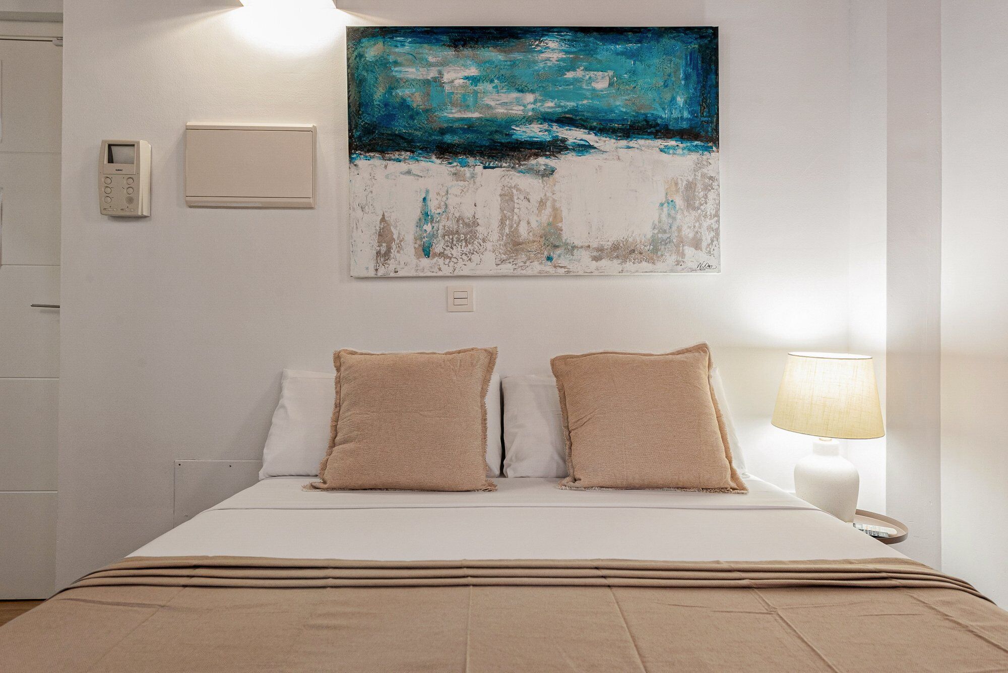 Une chambre d’hôtel avec un lit, deux oreillers, un tableau, un thermostat et une lampe.