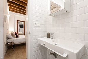 Une salle de bain moderne avec des carreaux de céramique blancs rectangulaires, un lavabo blanc avec un robinet chromé et un plafond en bois.
