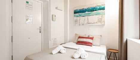 A hotel room with a bed, a painting, a door with a sign, and a small stool.