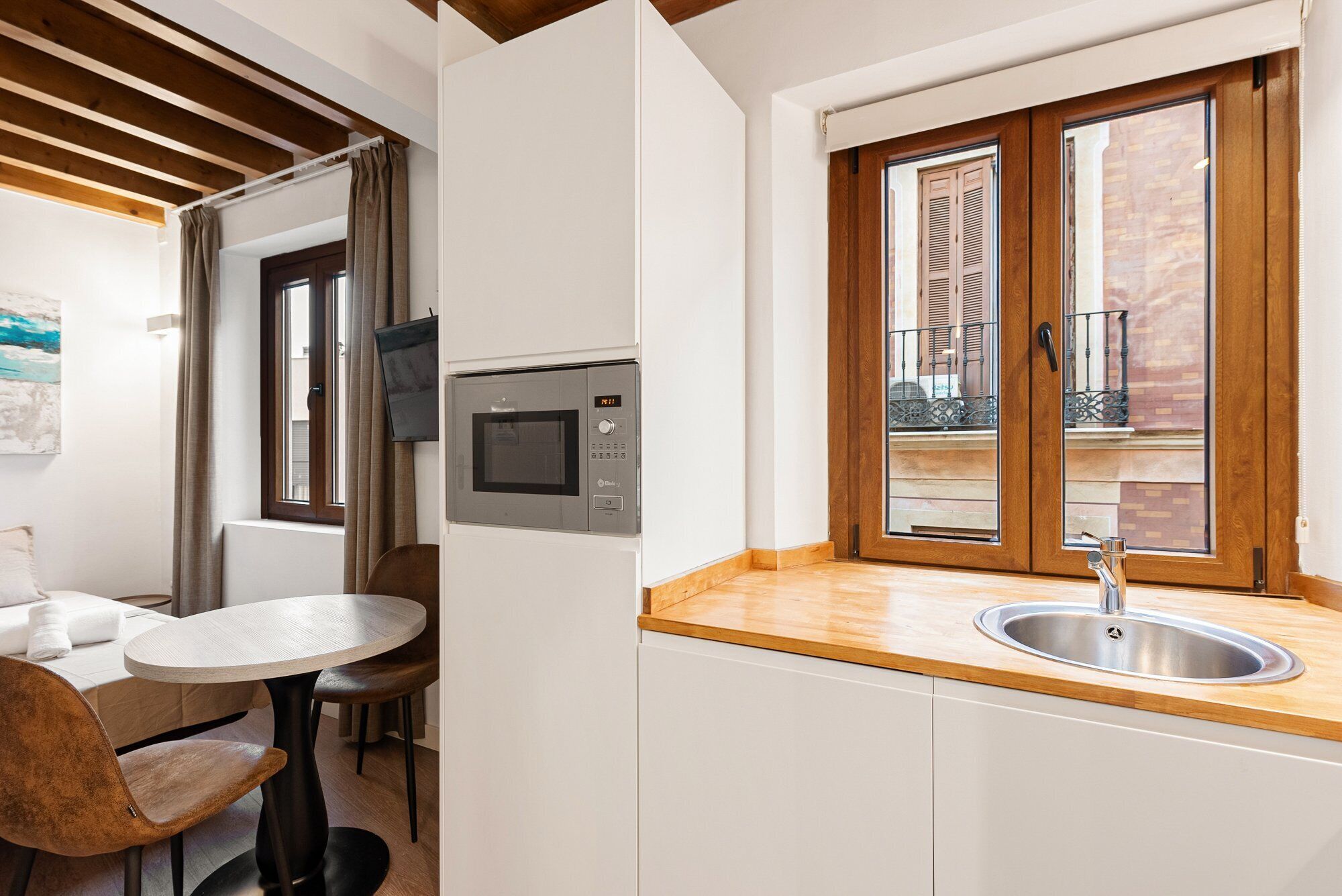 Une cuisine compacte dotée d’un four à micro-ondes encastré, d’un plan de travail en bois et d’un évier.