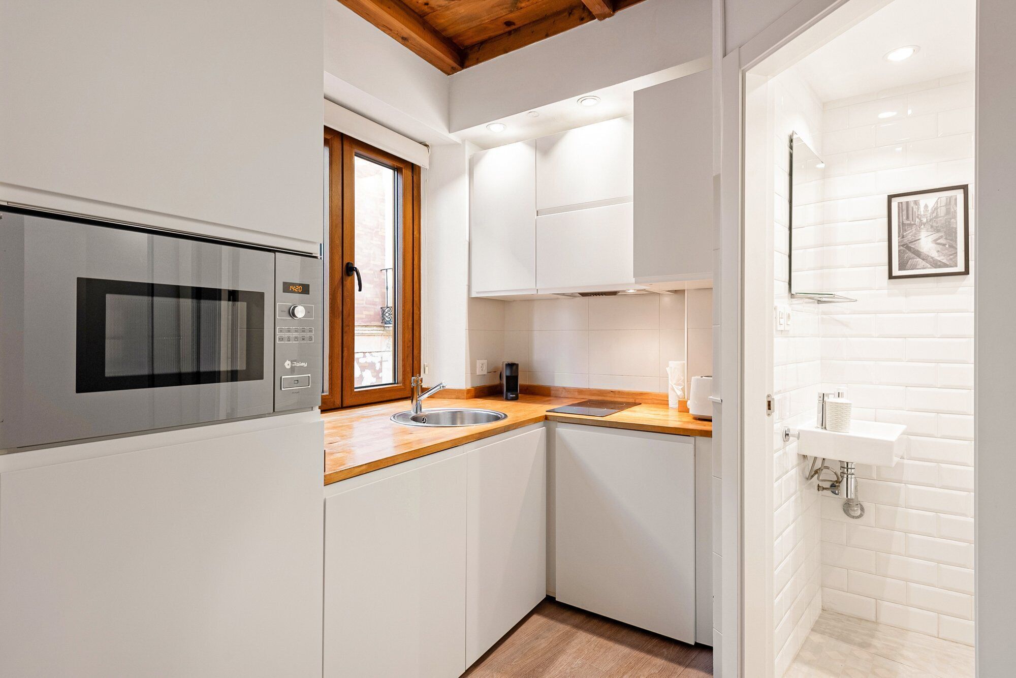 A modern kitchen with white cabinets, a wooden countertop, a built-in microwave, and a window with a view.