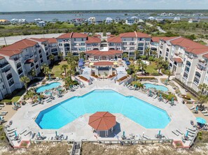 A resort with multiple buildings, a central swimming pool, and a view of the water.