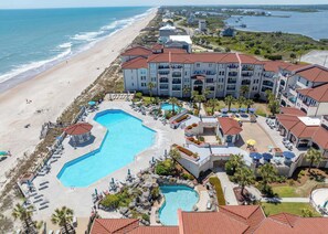 Un resort con varias piscinas, vistas a la playa y un edificio grande con balcones.