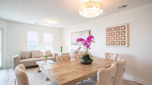 A dining area with a wooden table, beige upholstered chairs, and a chandelier.