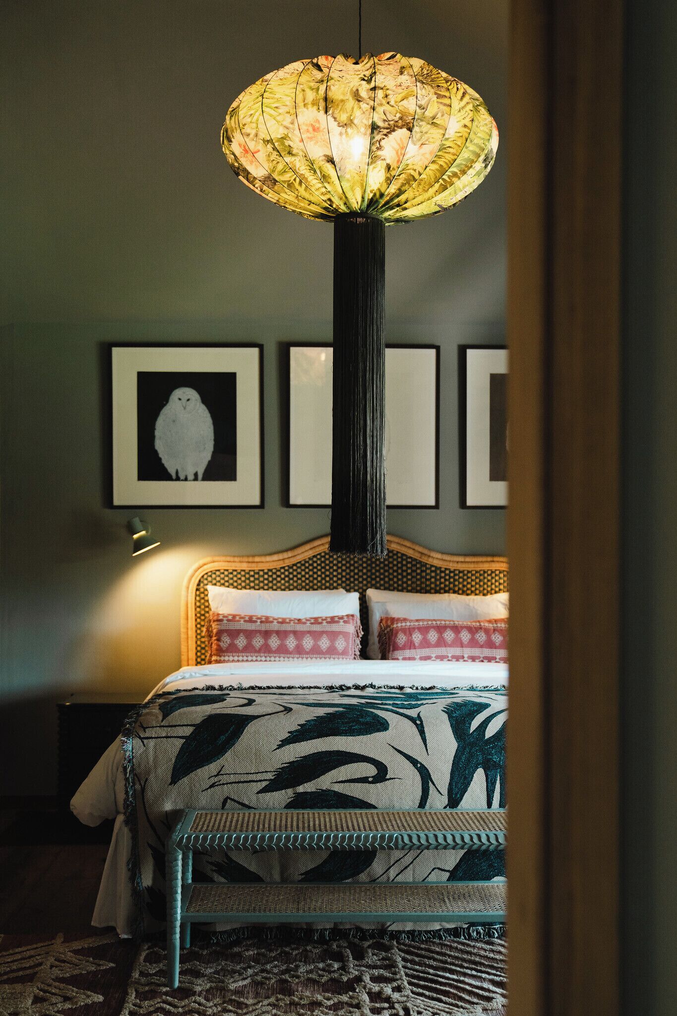 A bedroom with a bed, a hanging lamp, and framed pictures on the wall.