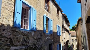 Una calle estrecha con edificios de piedra, contraventanas azules y un cielo azul despejado.