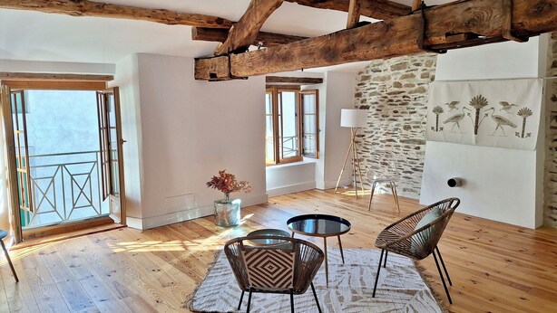 Una habitación amplia con pisos de madera, techo alto con vigas a la vista, pared de piedra y balcón con vistas.