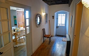 Un couloir étroit avec un plancher en bois, une chaise en bois, une porte avec une fenêtre et un luminaire fixé au mur.