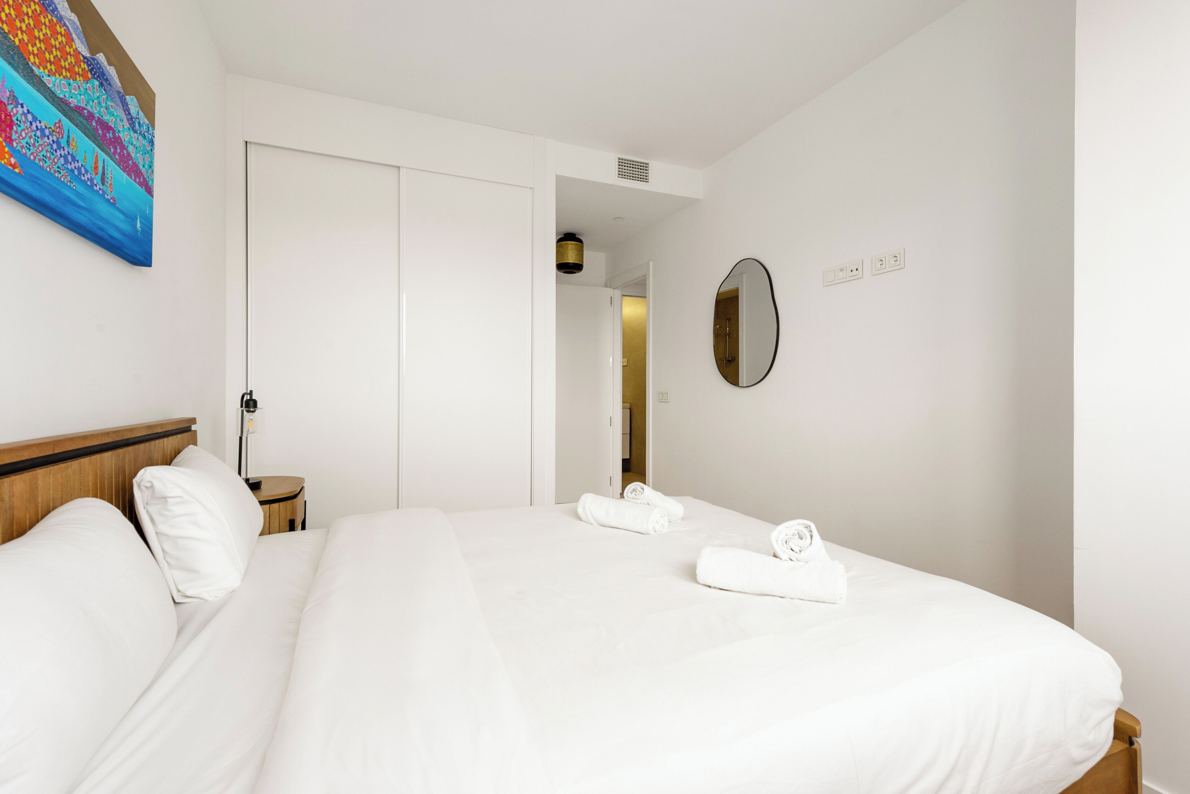 Une chambre d’hôtel avec un grand lit, une table de chevet, un miroir et un tableau au mur.
