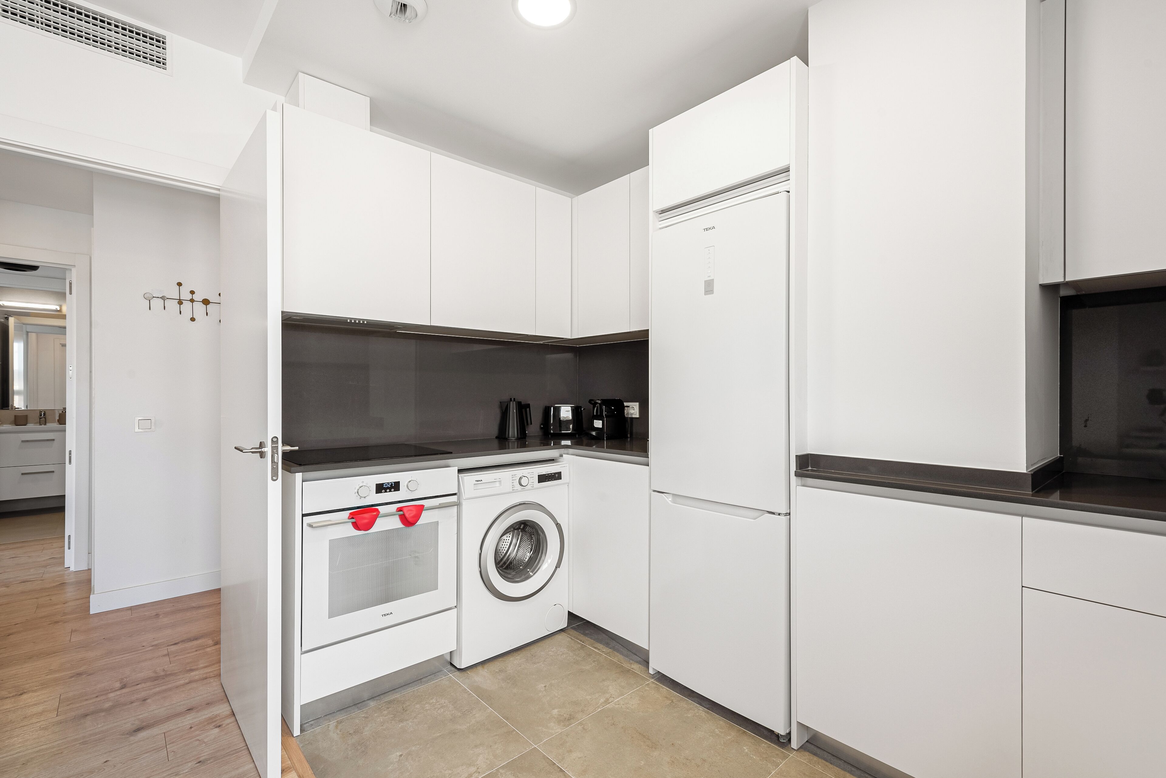 A modern kitchen with white cabinetry, a built-in washer and dryer, and a stainless steel range hood.