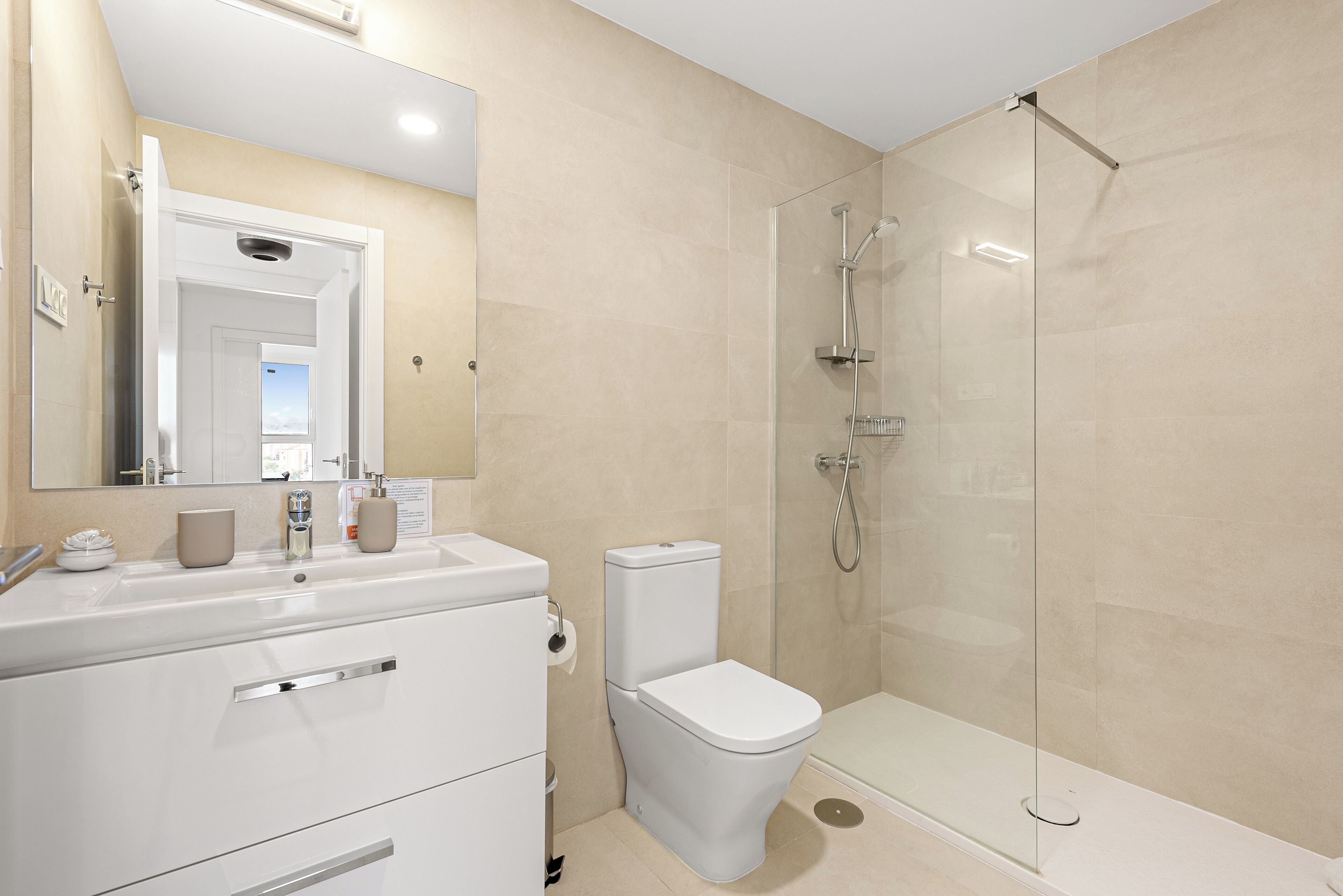Une salle de bain moderne avec un meuble-lavabo blanc, des toilettes et une douche séparée par une paroi de verre.