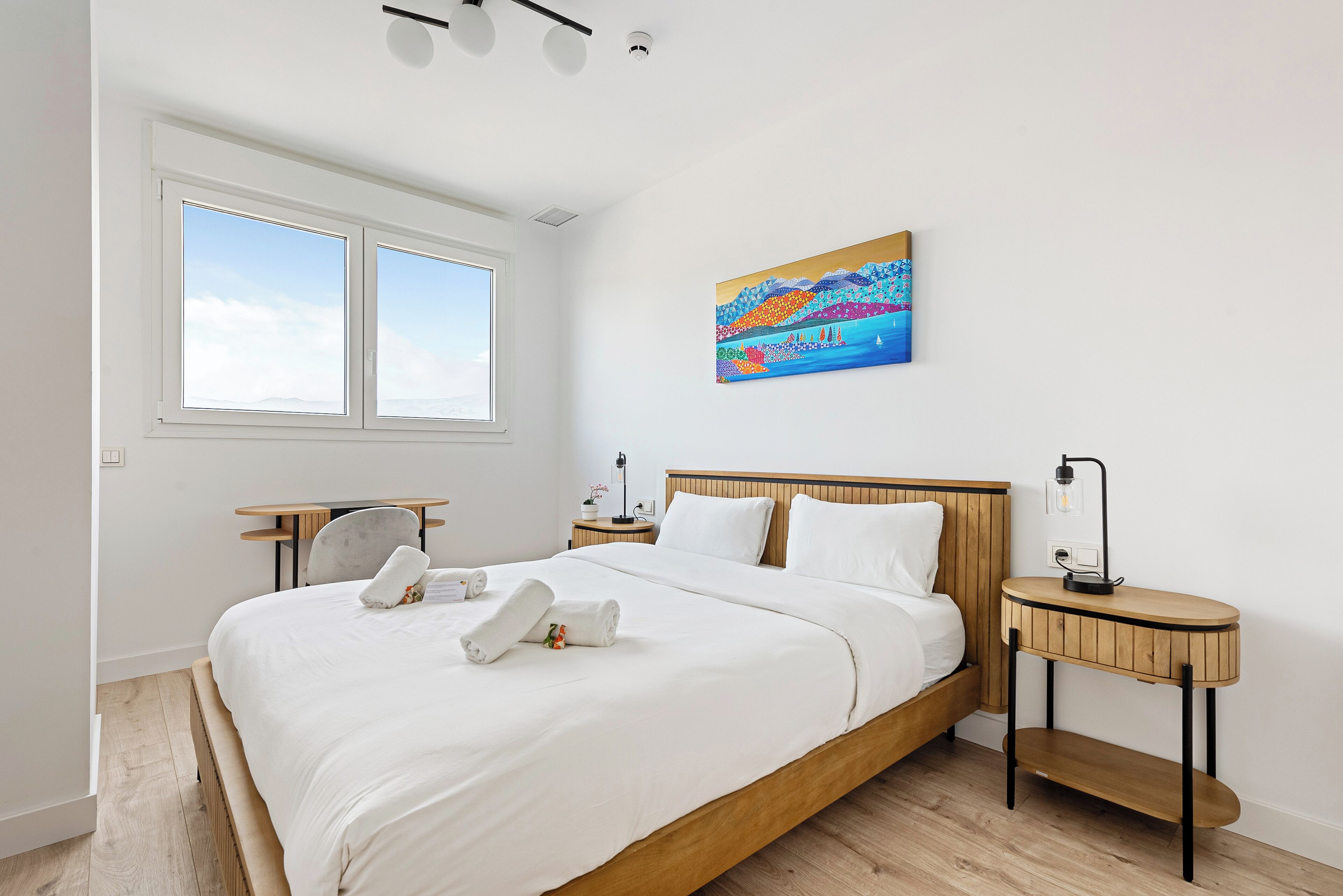 Un dormitorio moderno con una cama grande, una mesita de noche y un cuadro, además de una ventana.
