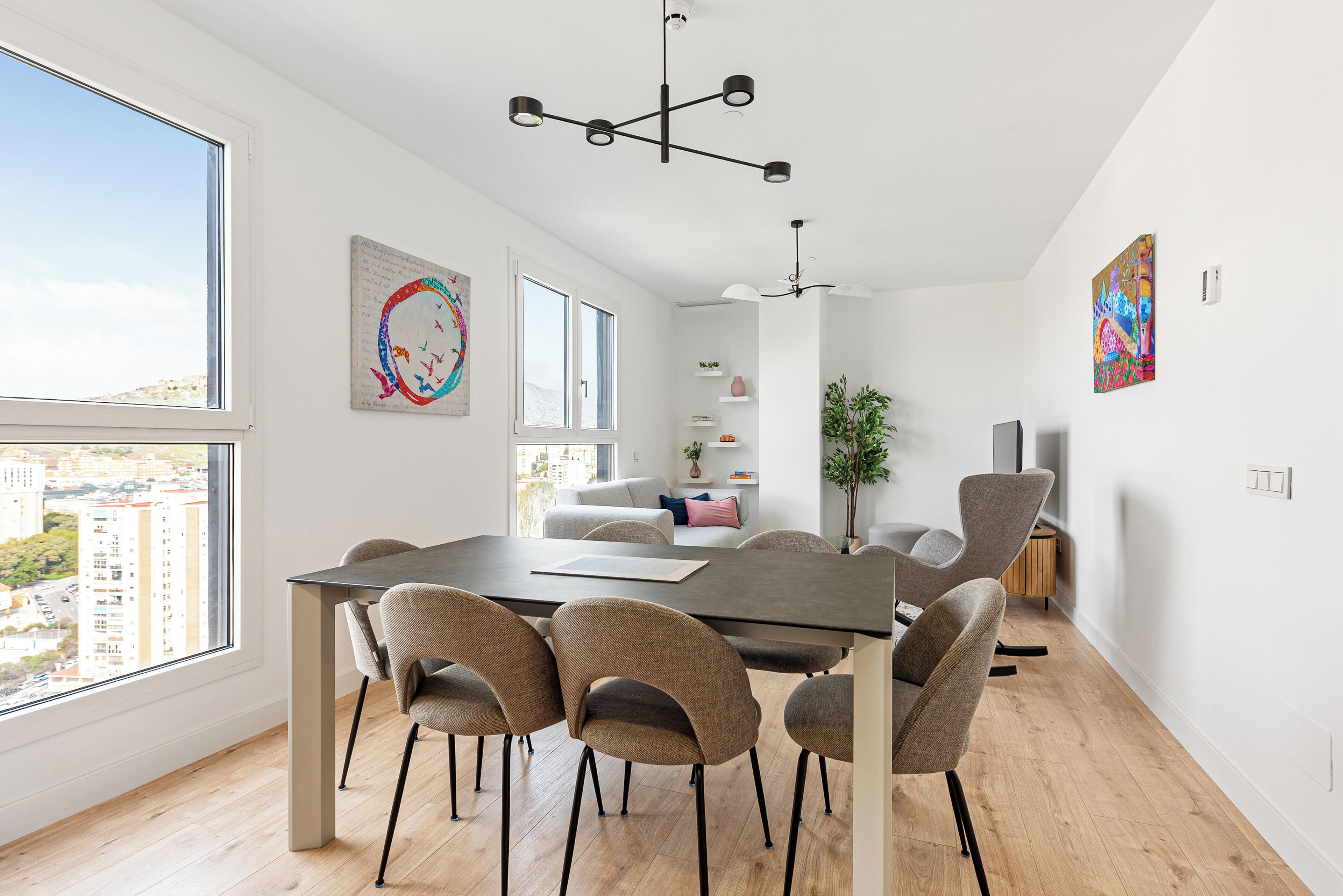 A modern dining area with a large table, six chairs, and a city view through a large window.