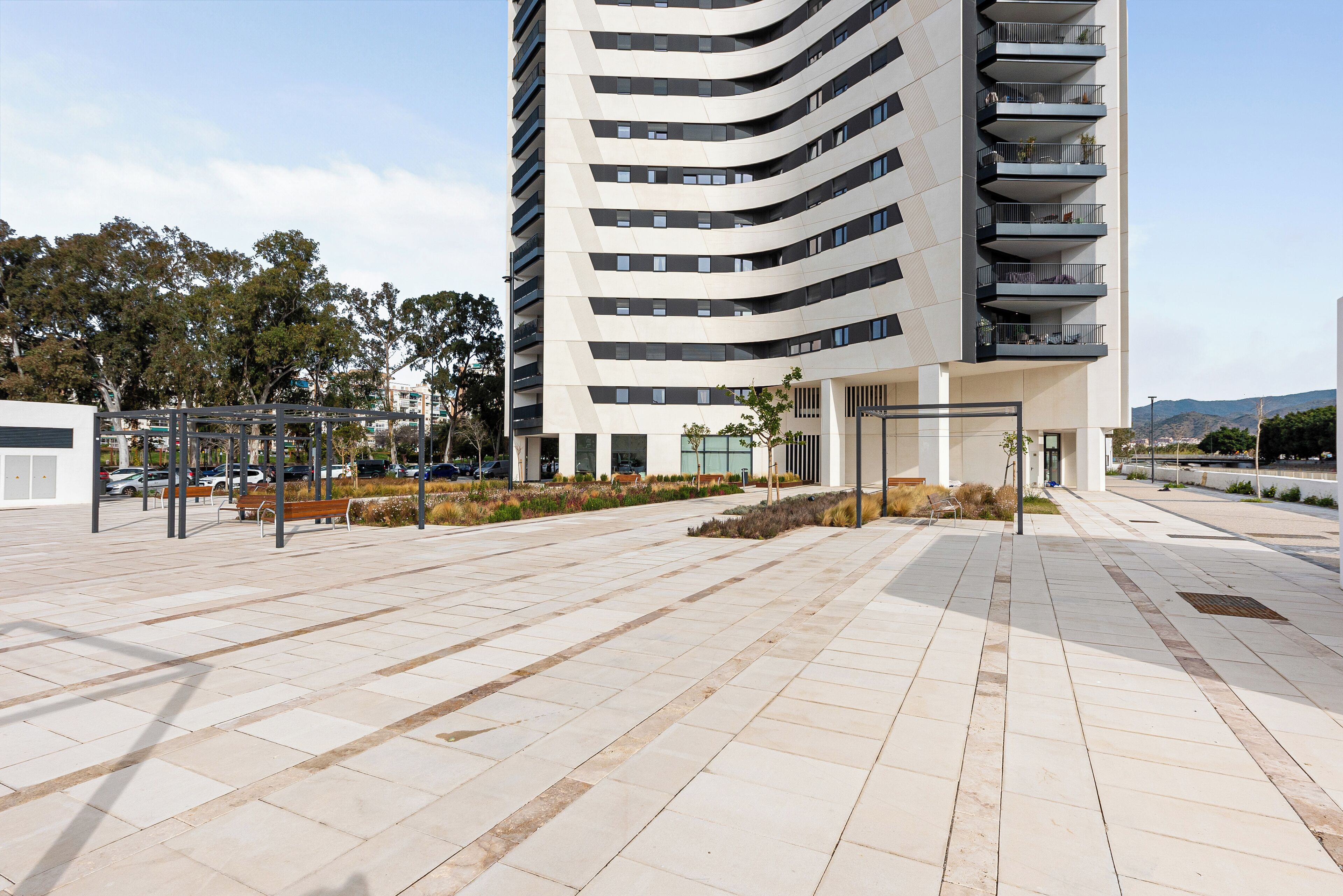 Een modern gebouw met een gebogen gevel, meerdere balkons en een ruim buitengebied met een betegeld pad.