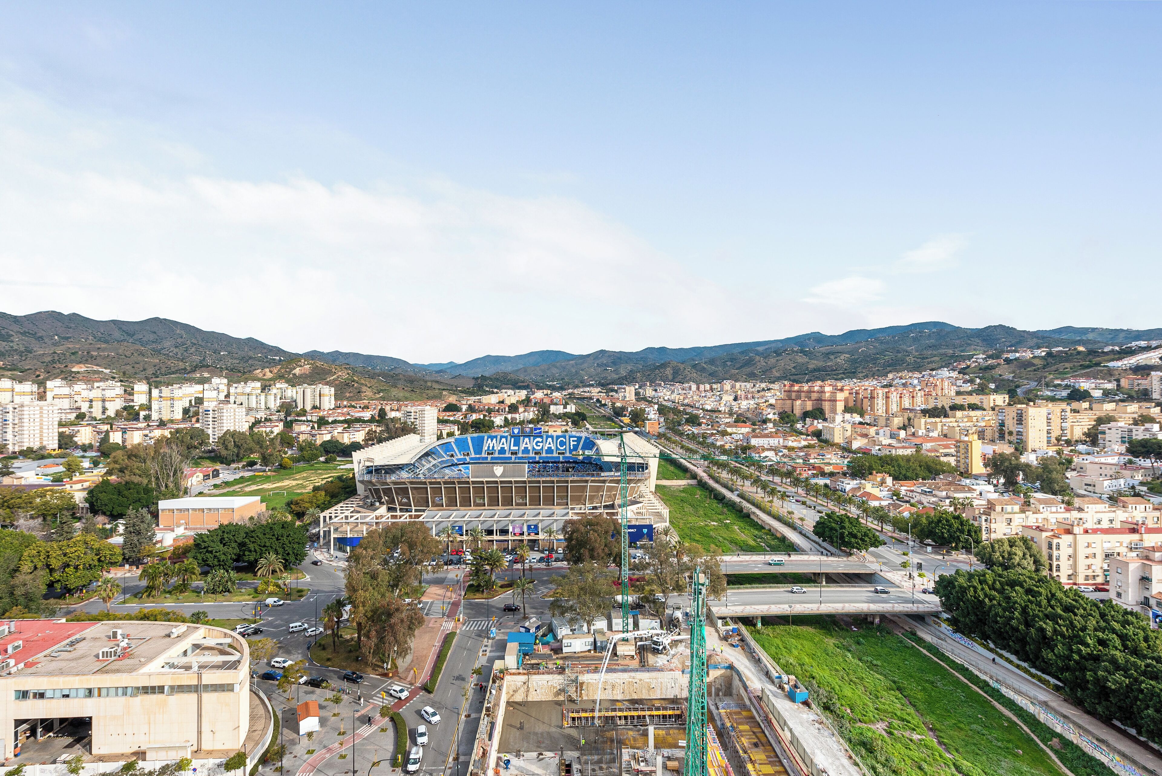A stadium with a large blue sign, surrounded by urban buildings and greenery.
