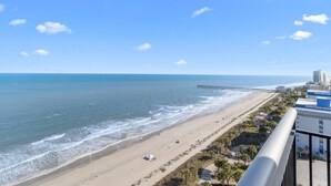 Vista sulla spiaggia con un molo che si protende sull'oceano, una spiaggia sabbiosa e una fila di edifici con balconi.