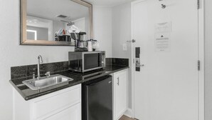 A compact kitchen with a sink, a microwave, a refrigerator, and a door with a notice. - Sunrise Serenity Oceanview Deluxe Double Room (Myrtle Beach)