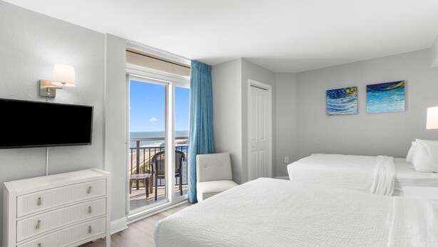A hotel room with a balcony, a TV, a white dresser, and two beds. - Sunrise Serenity Oceanview Deluxe Double Room (Myrtle Beach)