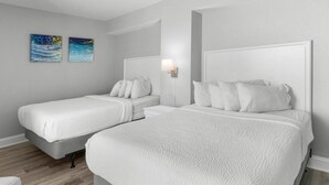 A hotel room with two beds, a nightstand, a lamp, and two paintings on the wall. - Sunrise Serenity Oceanview Deluxe Double Room (Myrtle Beach)