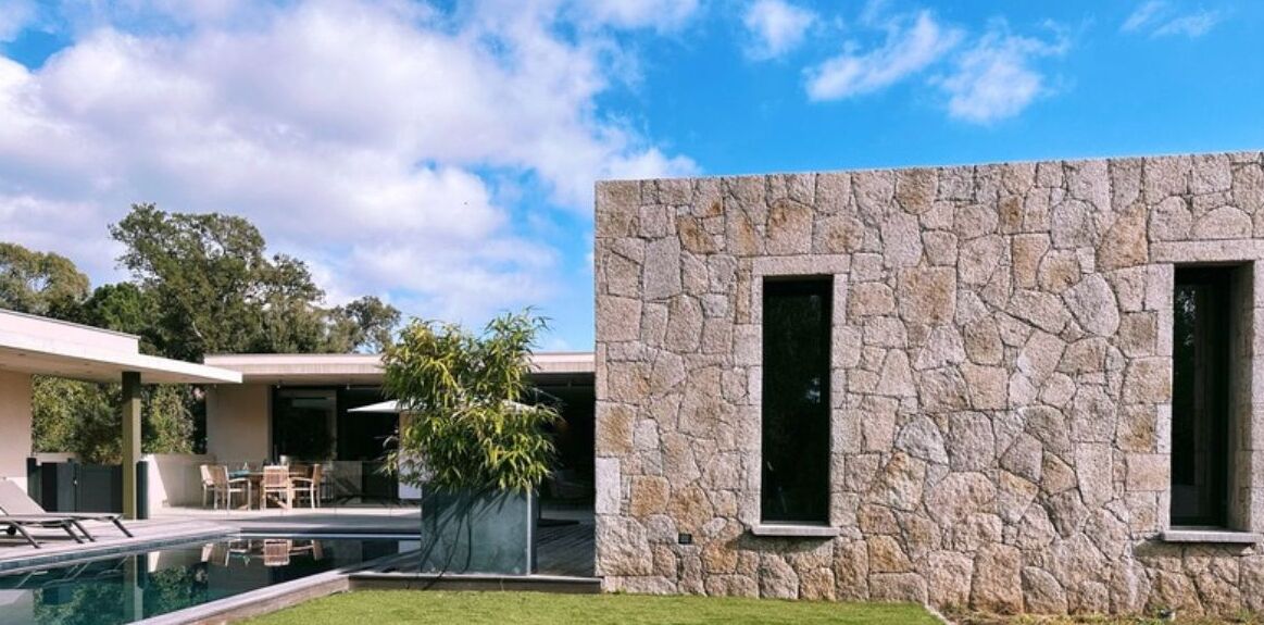 A modern house with a stone facade, a swimming pool, and a patio area.