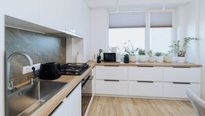 A modern kitchen with white cabinets, a stainless steel sink, a wooden countertop, and a window with blinds.