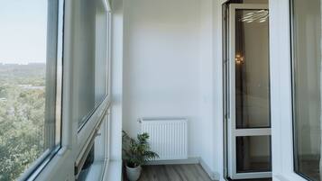 A balcony with a view of trees and buildings, a potted plant, a white radiator, and a sliding glass door.