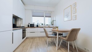 A modern kitchen with white cabinetry, a wooden countertop, and a dining area with two chairs.