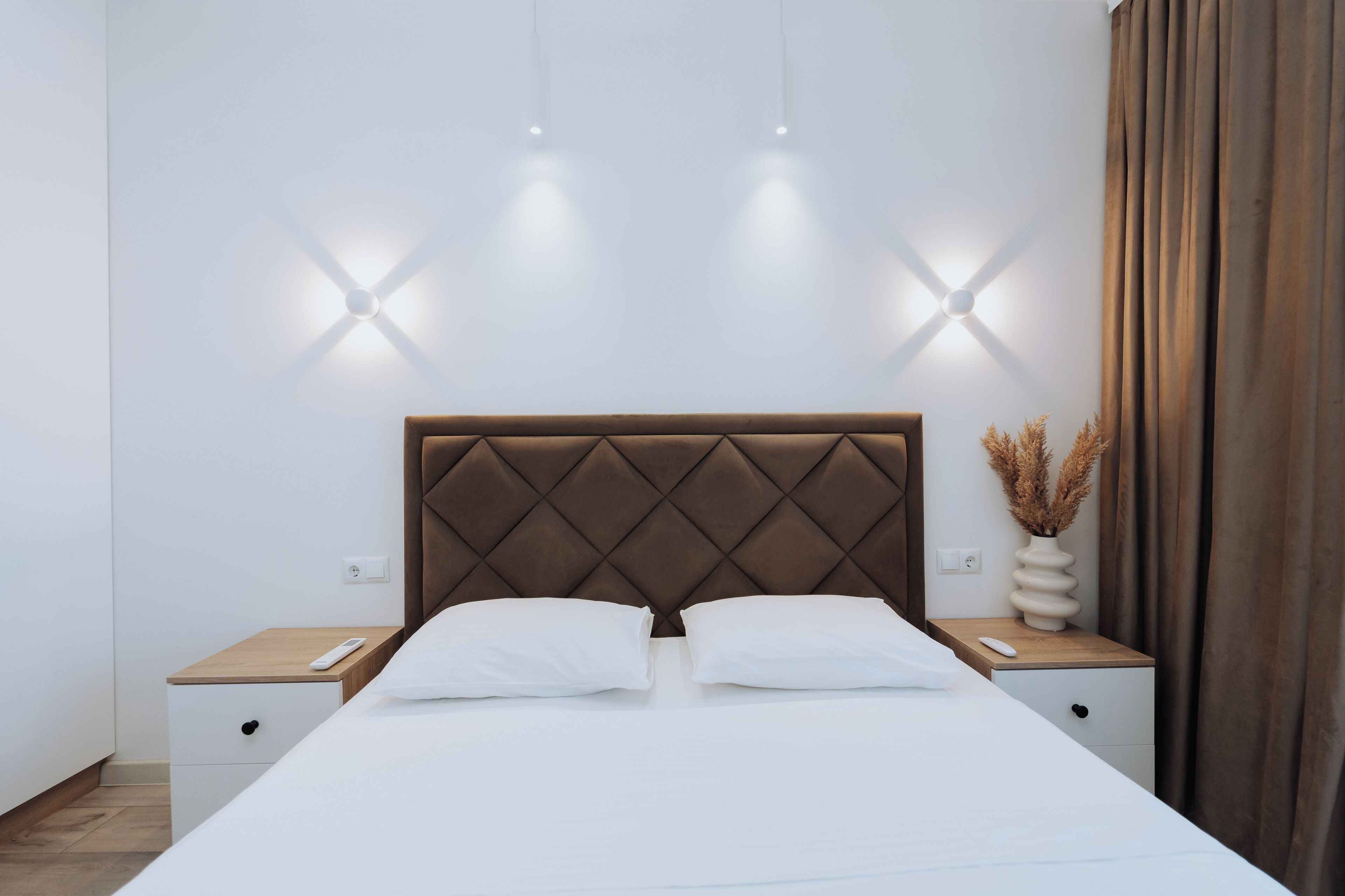 A modern hotel room with a large bed, two bedside tables, and a wall-mounted light fixture.
