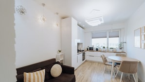 A modern kitchen with white cabinets, a dining area with a table and chairs, and a living space with a brown sofa and decorative pillows.