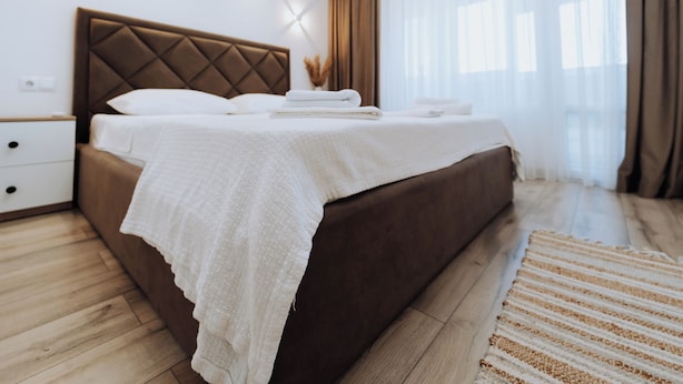 A modern bedroom with a large bed, a nightstand, and a wooden floor.
